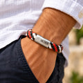 Stoere rood zwart witte gevlochten leren herenarmband met zilverkleurige metalen sluiting, gedragen om de pols van een man.